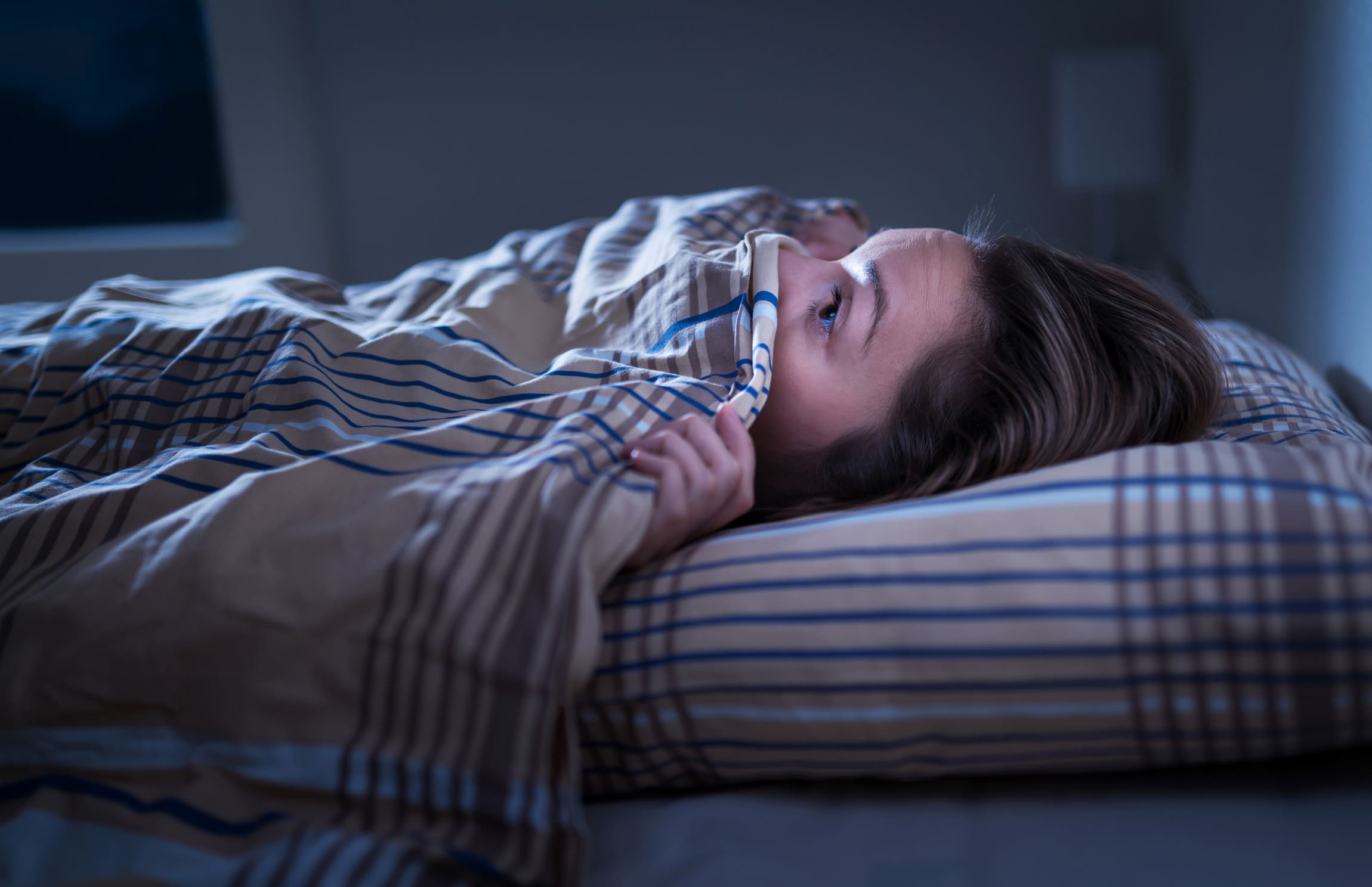 woman lying under the covers in the dark scared to come out