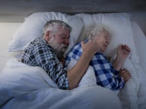 older couple sleeping together in plaid shirts on comfy bed