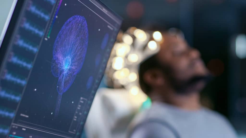 man sitting in a chair with eyes closed and hooked up to machine showing the brain at rest