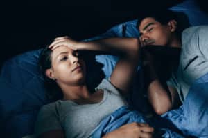 Annoyed woman lying in bed with snoring boyfriend at home in the bedroom. She needs a mattress to prevent snoring.