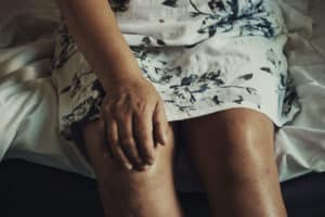 woman in dress on a bed with her hand on her knee because of joint pain